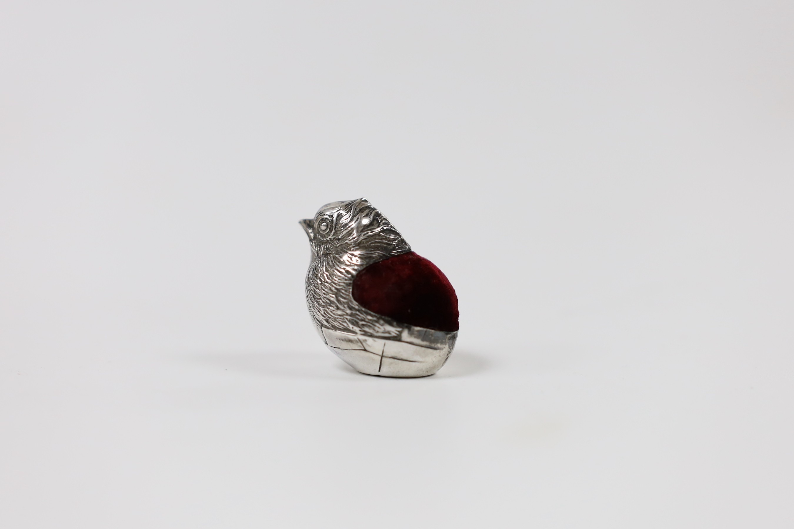An early 20th century novelty silver mounted pin cushion, modelled as a hatching chick, Chester, 19??, maker's mark and date letter rubbed, height 36mm.